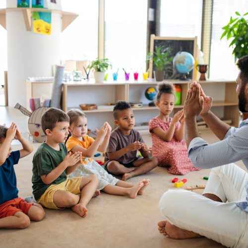 A group of small nursery school children with man teacher sitting on floor indoors in classroom, playing.